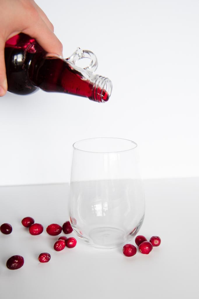 cranberry syrup bring poured into a glass with fresh cranberries around it 