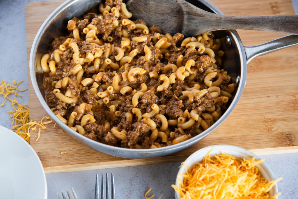 a pan of hamburger helper with a bowl of cheese next to it 