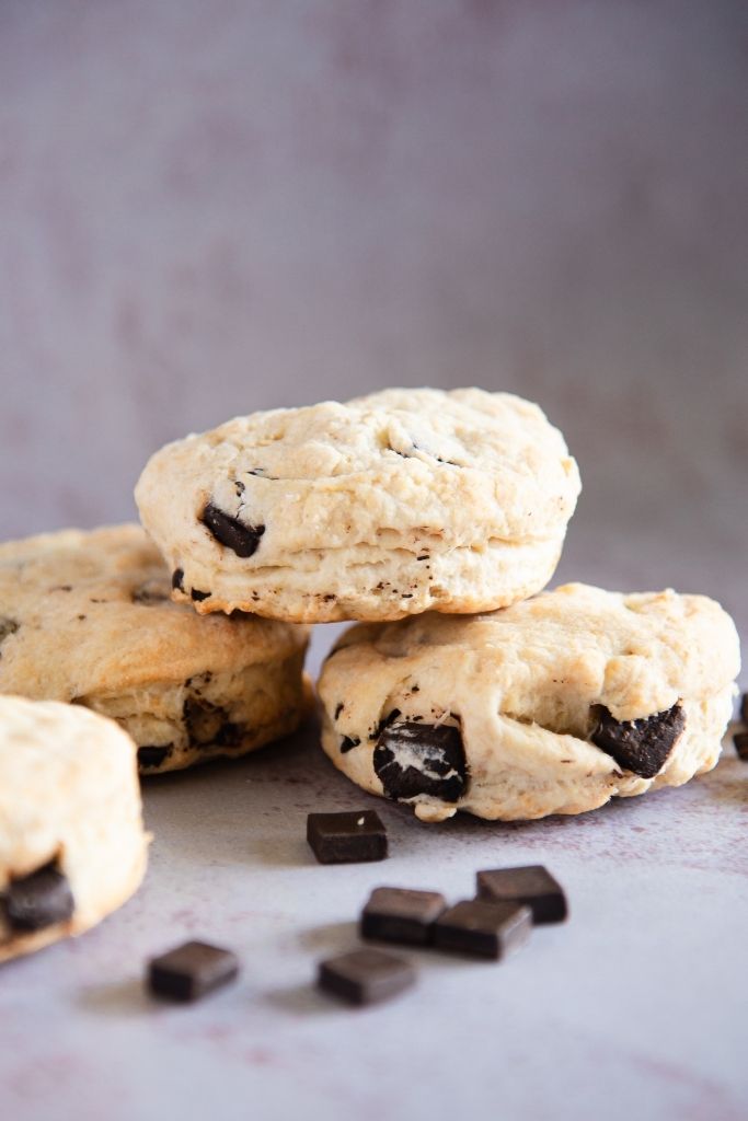 a biscuit set on top of two other biscuits with chocolate chunks sprinkled in front of them