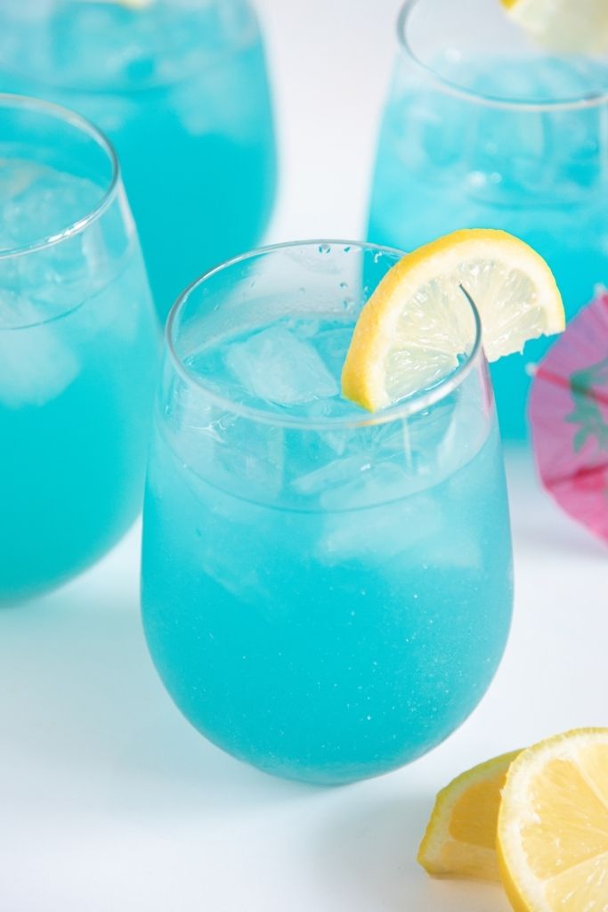 a glass of lemonade with lemon slices next to it, you can see three other glass behind it 