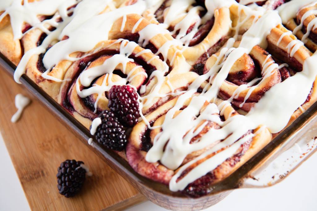 a pan of sweet rolls on a wooden cutting board 