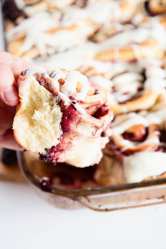 someone holding a sweet roll in front of a pan of sweet rolls