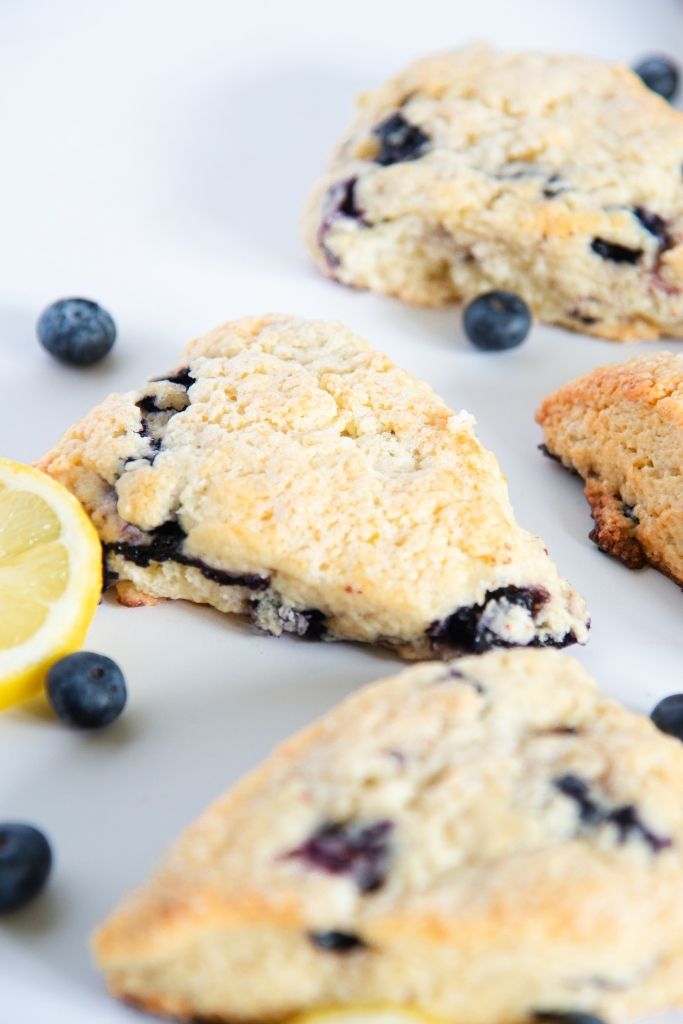 a close up of a blueberry lemon scone with a lemon slice and some blueberries next to it 