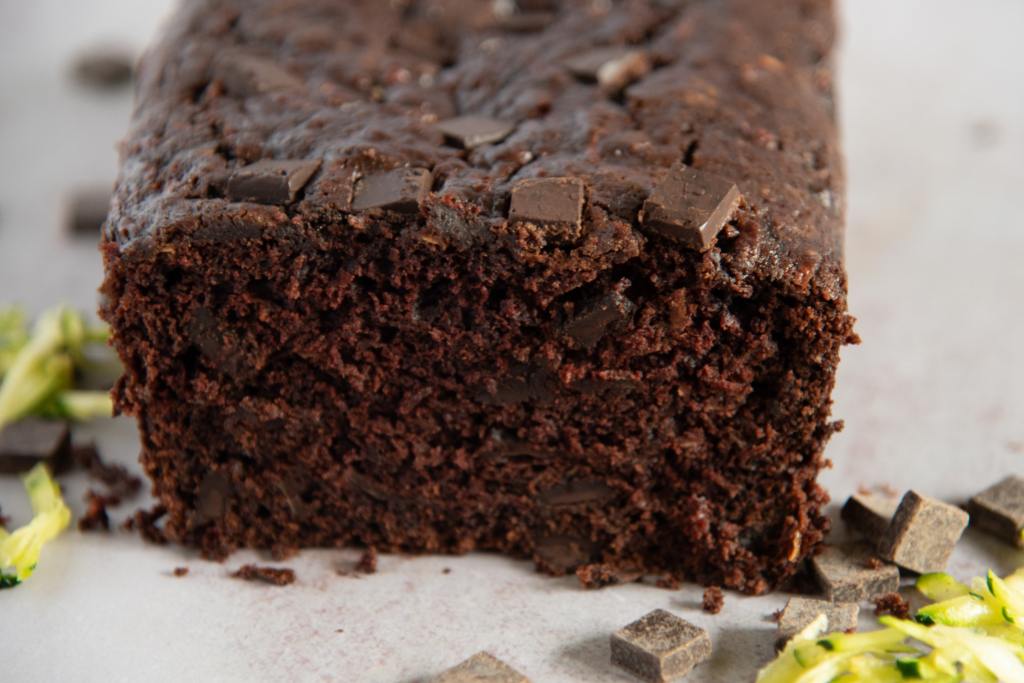 a cut loaf of bread with shredded zucchini and chocolate chunks next to it