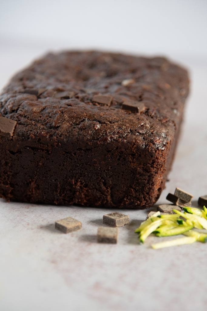a loaf of bread with shredded zucchini and chocolate chunks next to it