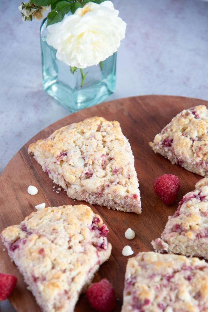 a close up on a raspberry white chocolate scone with a white rose next to it 