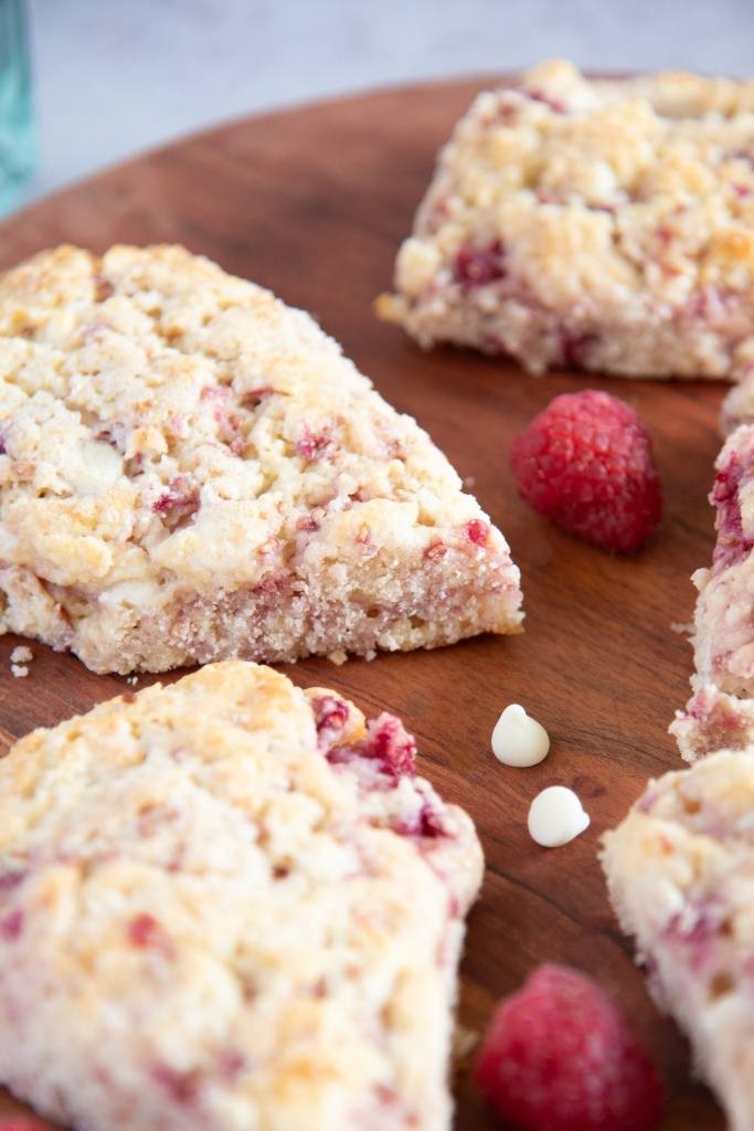 a close up of scones on a wooden plate, there are fresh raspberries and chocolate chips on the plate as well