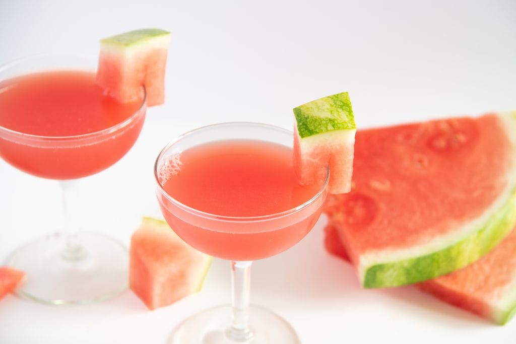 two finished cocktails with watermelon slices next to them 