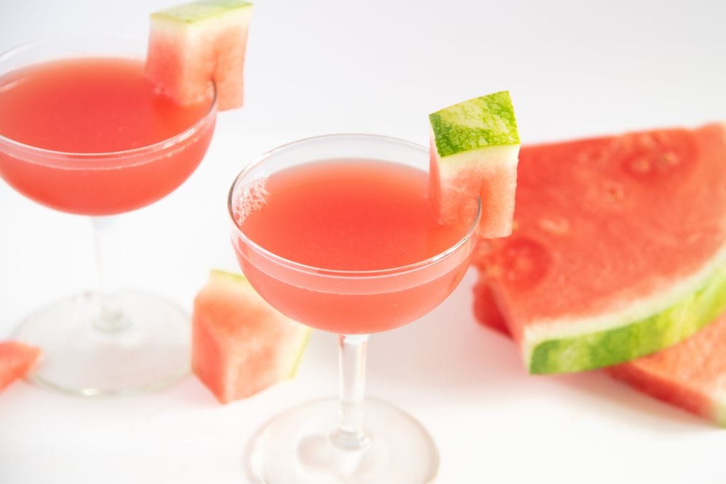 two finished cocktails with watermelon slices next to them 