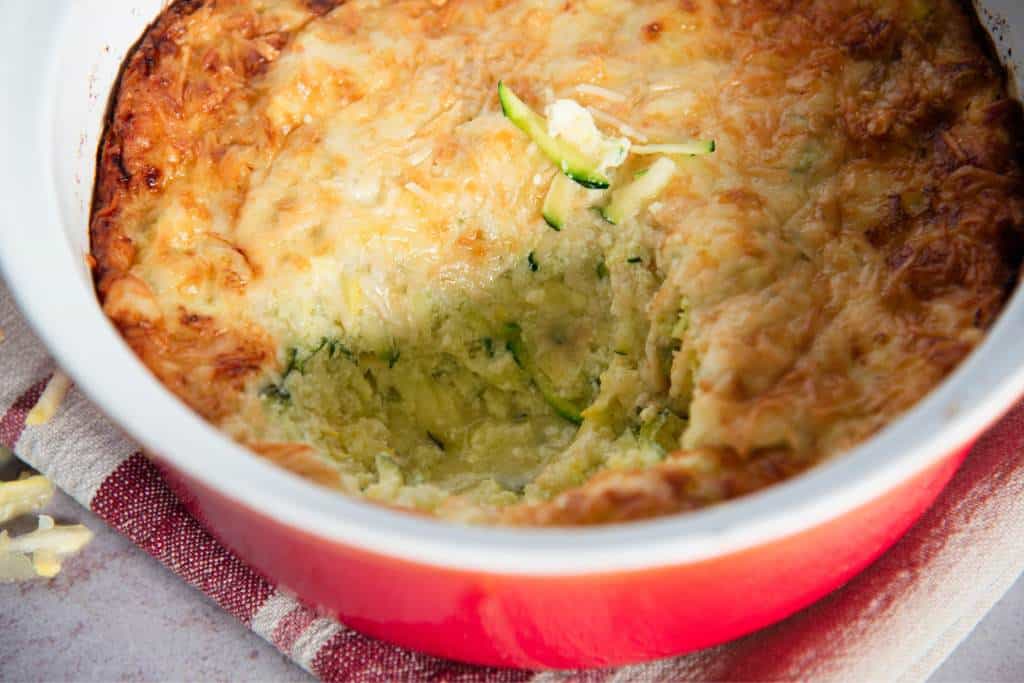 a close up of a dish of casserole that has a spoonful taken out it