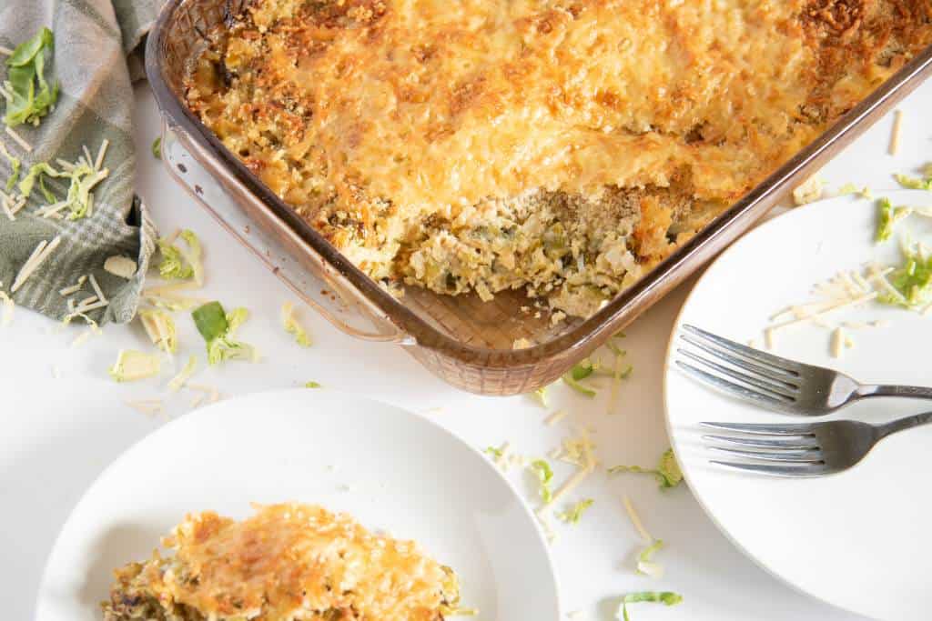 a pan of gratin with spoonful taken out of it, there are two plates and some forks next to the pan