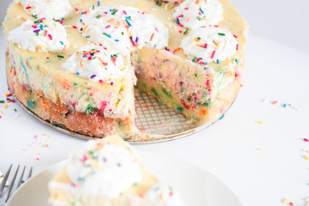 a cheesecake with a slice taken out of it, there is a slice of cheesecake on a plate in front of it.