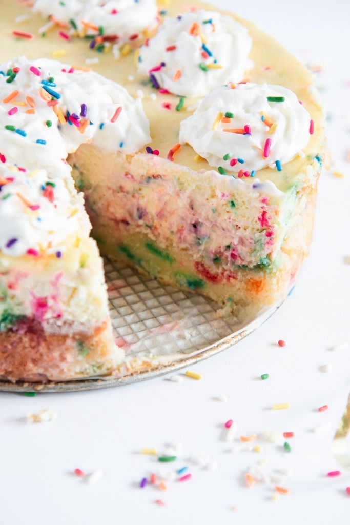 a birthday cake cheesecake with a slice taken out of it