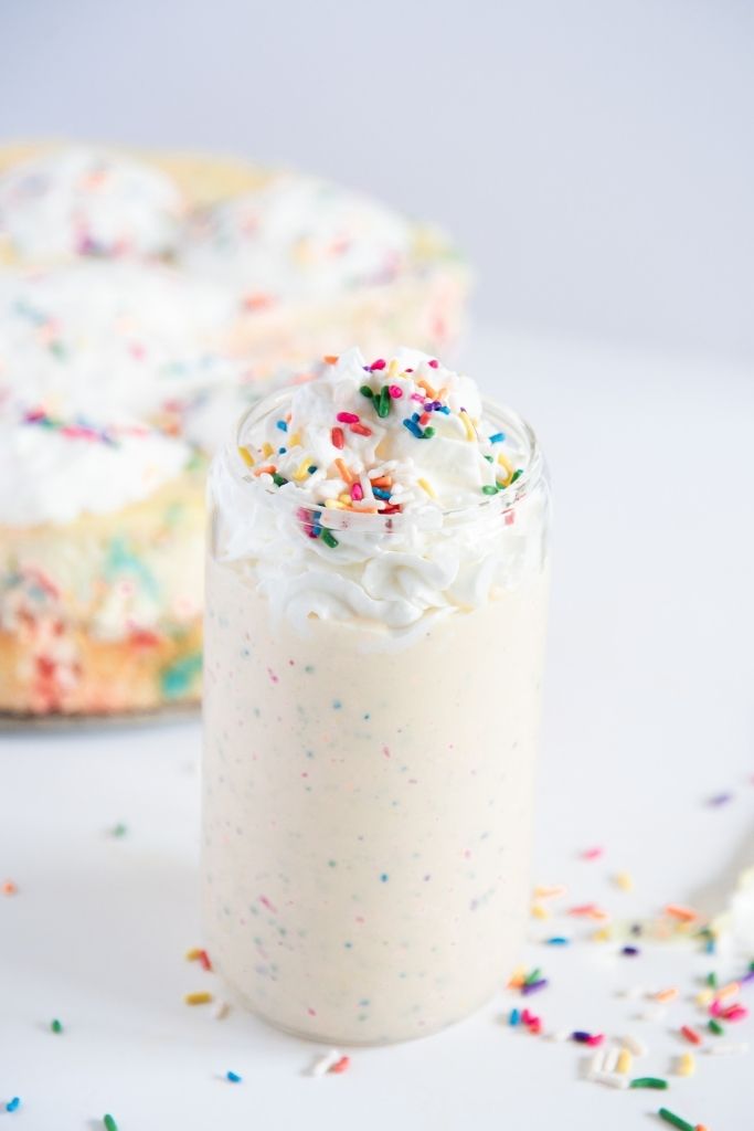 a birthday cake milkshake with a birthday cake behind it