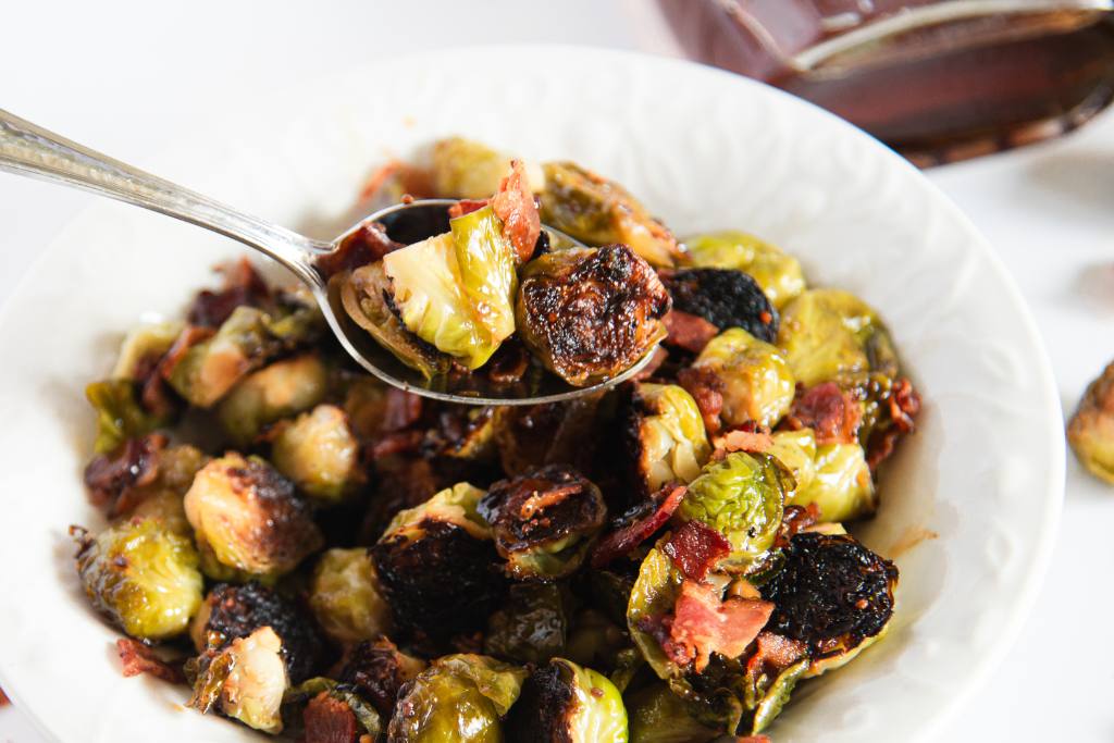 a spoonful of brussels sprouts being held over a dish of brussels sprouts 
