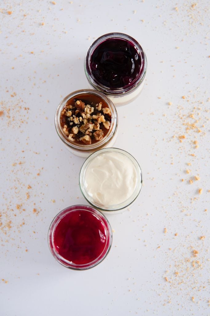four jars of cheesecake lined up, each one as a different topping