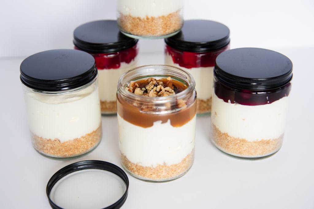 six jars of no back cheesecake, one jar has the lid off