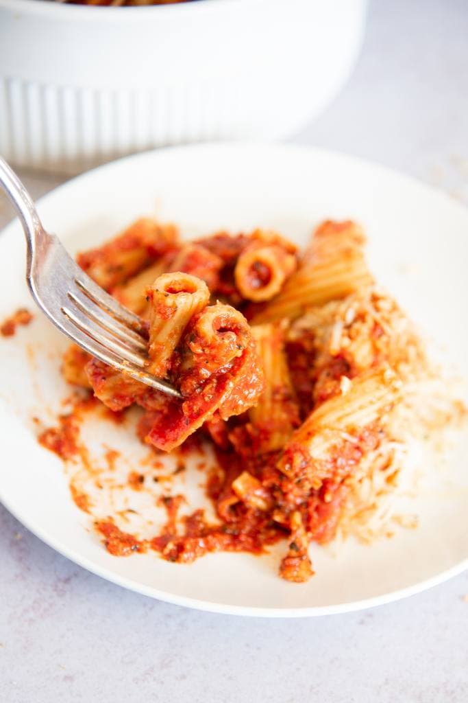 a fork full of pizza pasta being held over a plate of pizza pasta 