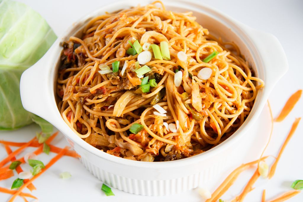 a dish of cabbage noodles, there are some carrots and a head of cabbage next to it 