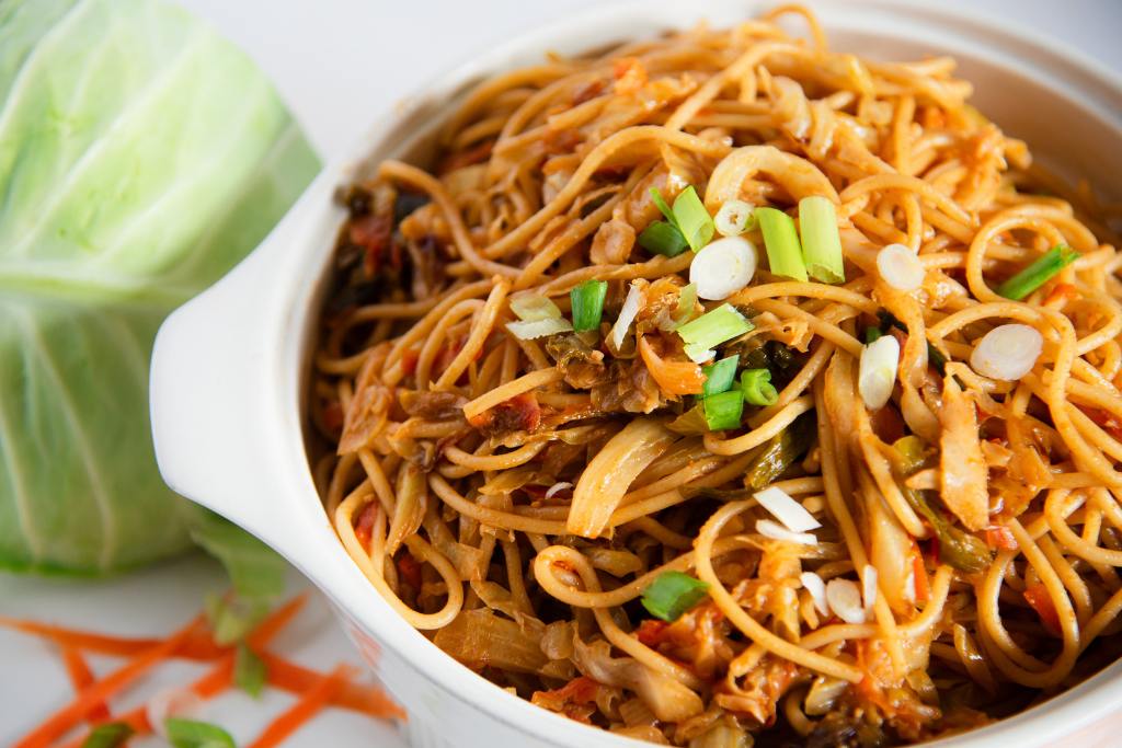 a close up of a dish of cabbage noodles with a head of cabbage next to it 
