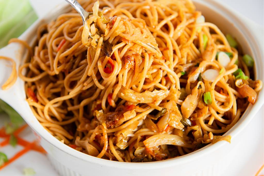 a fork full of noodles being held over a dish of noodles