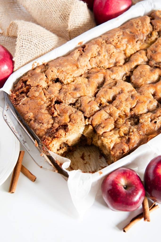 a pan of coffee cake with apples and cinnamon sticks around it