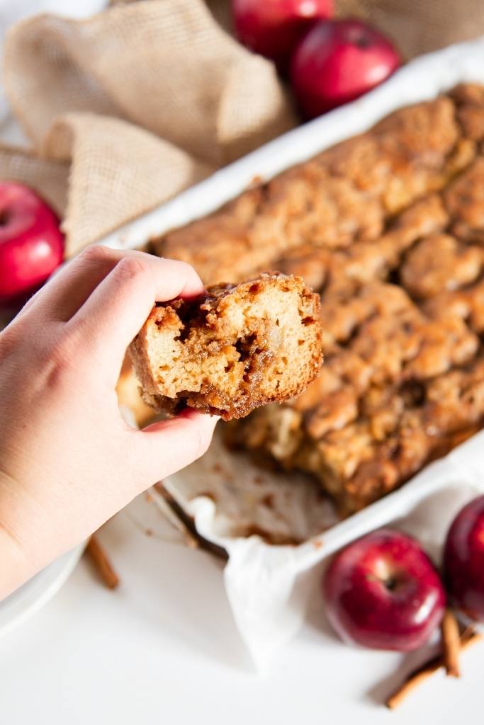a piece of coffee cake being held in front of a pan of coffee cake