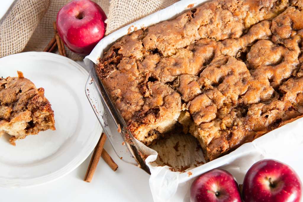 a pan of coffee cake with apples cinnamon sticks and a piece of coffee cake next to it