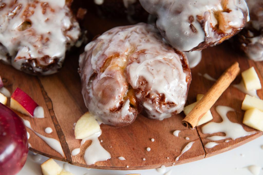 a close up on an apple fritter on a plate, with a cinnamon stick and apple pieces next to it 