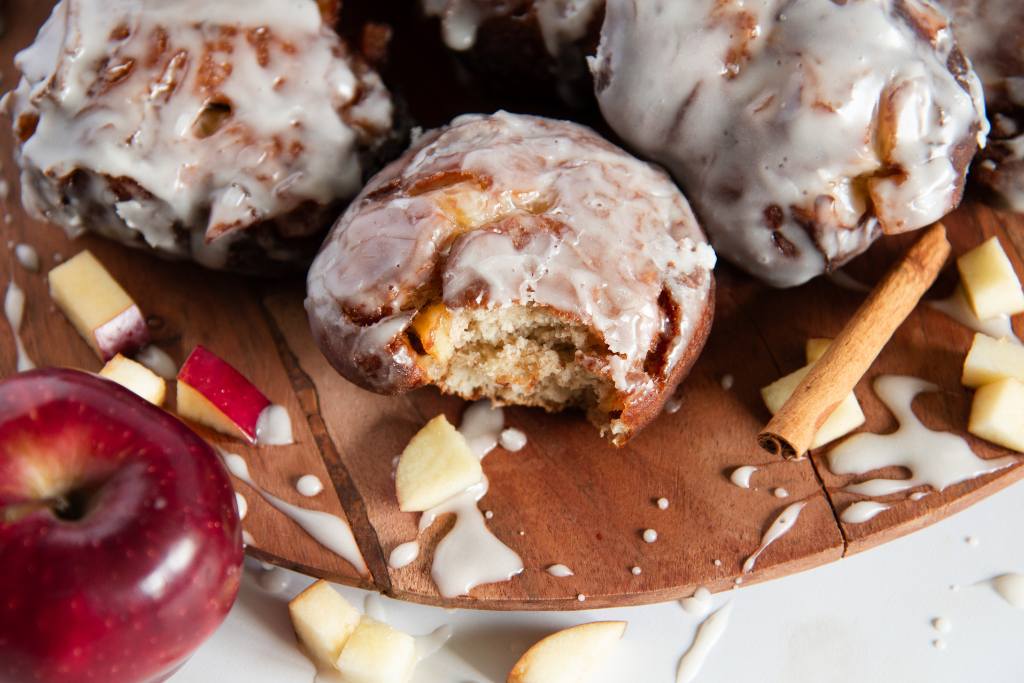 a plate of apple fritters, the fritter in front has a bite taken out of it 