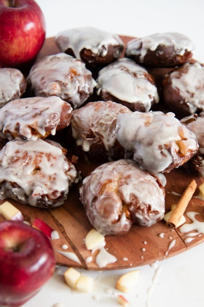 a plate of apple fritters with apple pieces and a whole apple next to them
