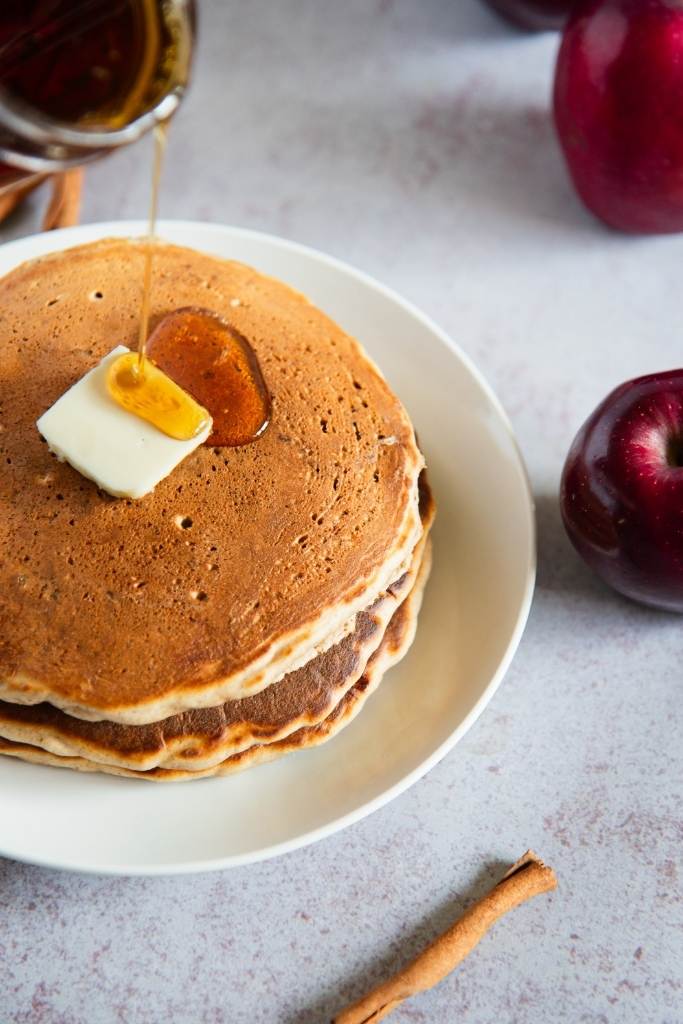 syrup starting to be poured unto a stack of pancakes 