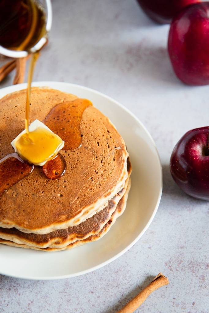 someone pouring syrup onto a stack of pancakes 