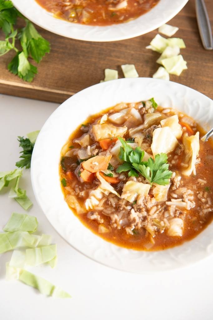 a bowl of cabbage roll soup with a spoon in it, you can see part of another bowl behind it too. 