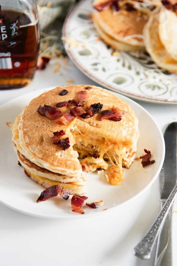 a plate of grilled cheese pancakes, you can see a bottle of syrup and more pancakes behind it