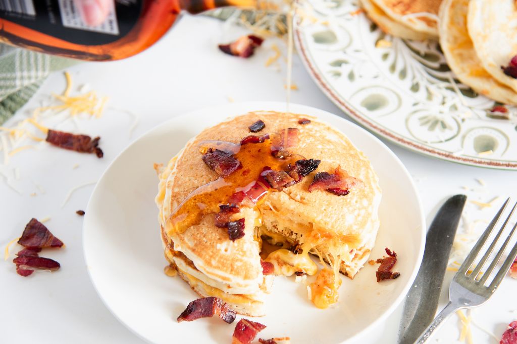someone pouring maple syrup onto a stack of grilled cheese pancakes