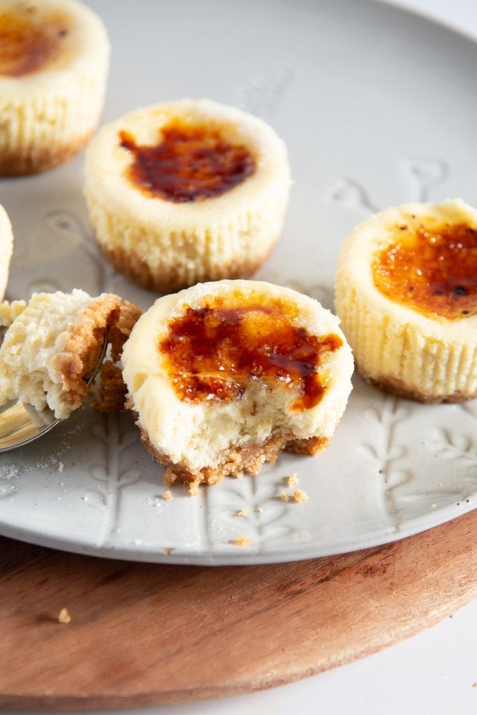 a mini cheesecake with a bite taken out of it, there is a forkful of cheesecake next to it