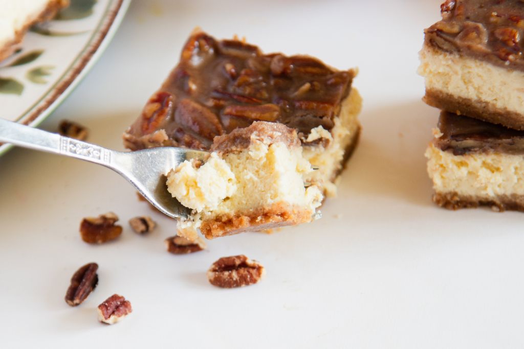 a forkful of cheesecake being held in front of cheesecake bar