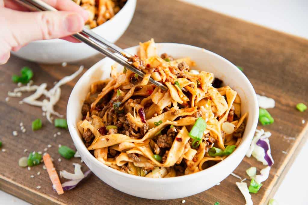 someone holding chopsticks full of noodles over a bowl of noodles