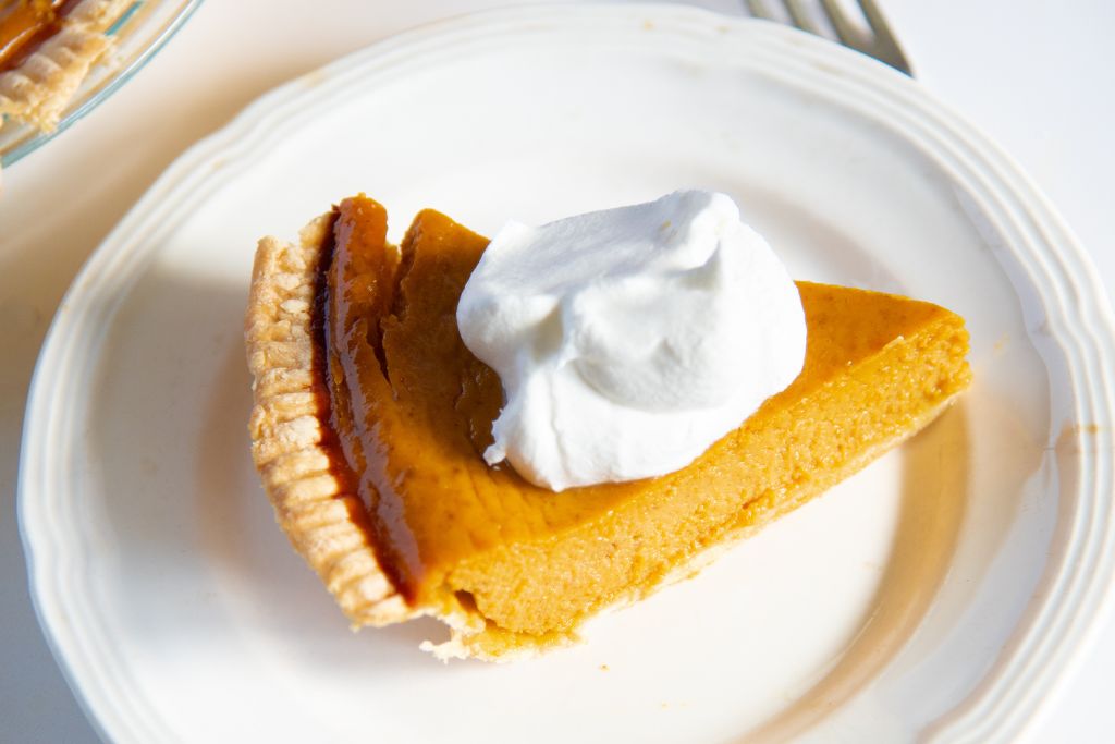 a close up of a piece of pumpkin pie on a plate, with whipped cream on top