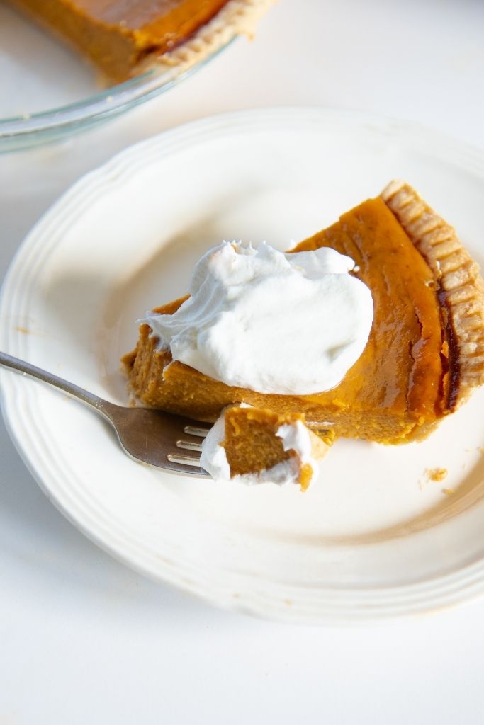 a piece of pie with whipped cream on a plate, with a forkful of pie sitting next to the piece
