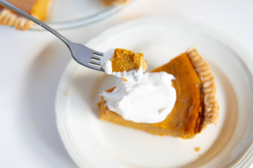 a forkful of pumpkin pie being held over a piece of pie