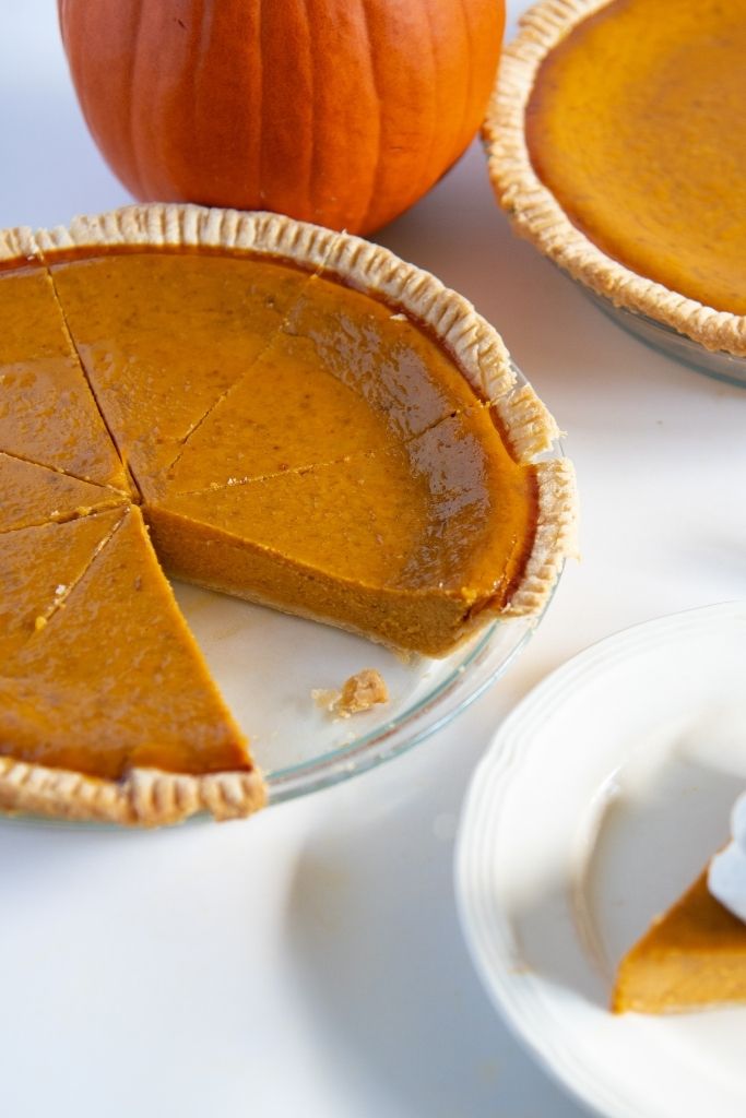a pumpkin pie with a slice taken out of it, there is another pie behind it