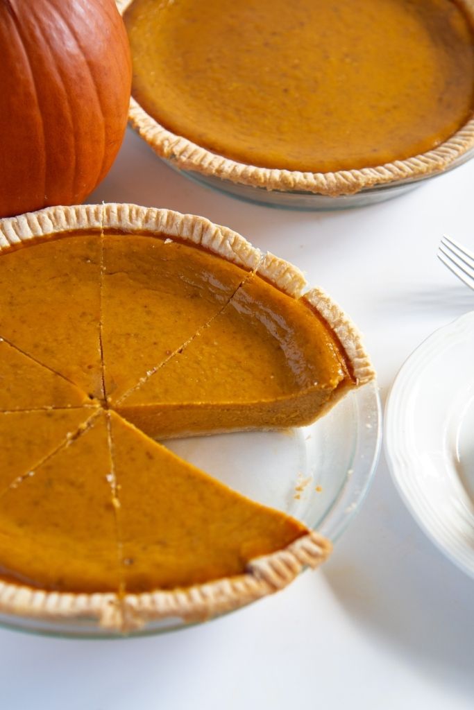 two pumpkin pies next to each other, one has a slice taken out of it
