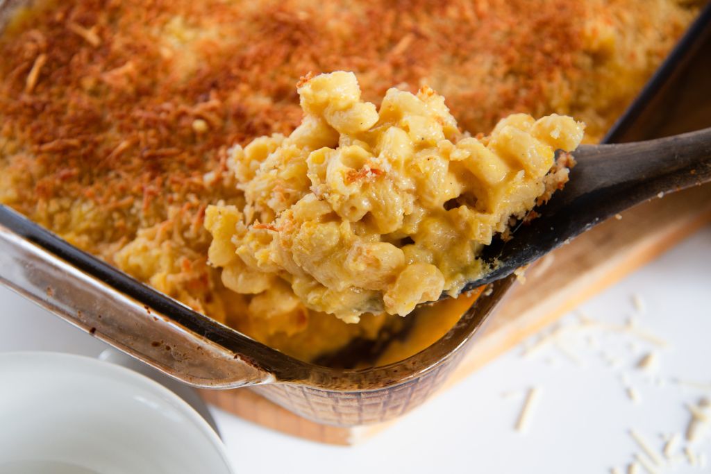 a spoonful of mac and cheese being held over a pan of mac and cheese