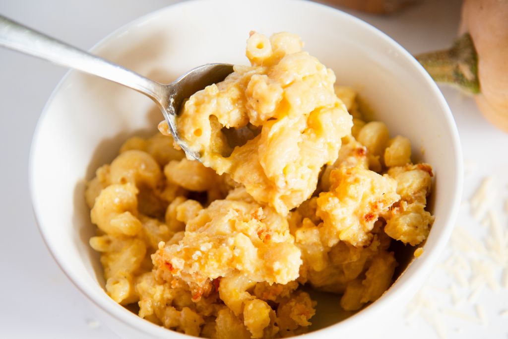 a spoonful of mac and cheese being held over a bowl of mac and cheese