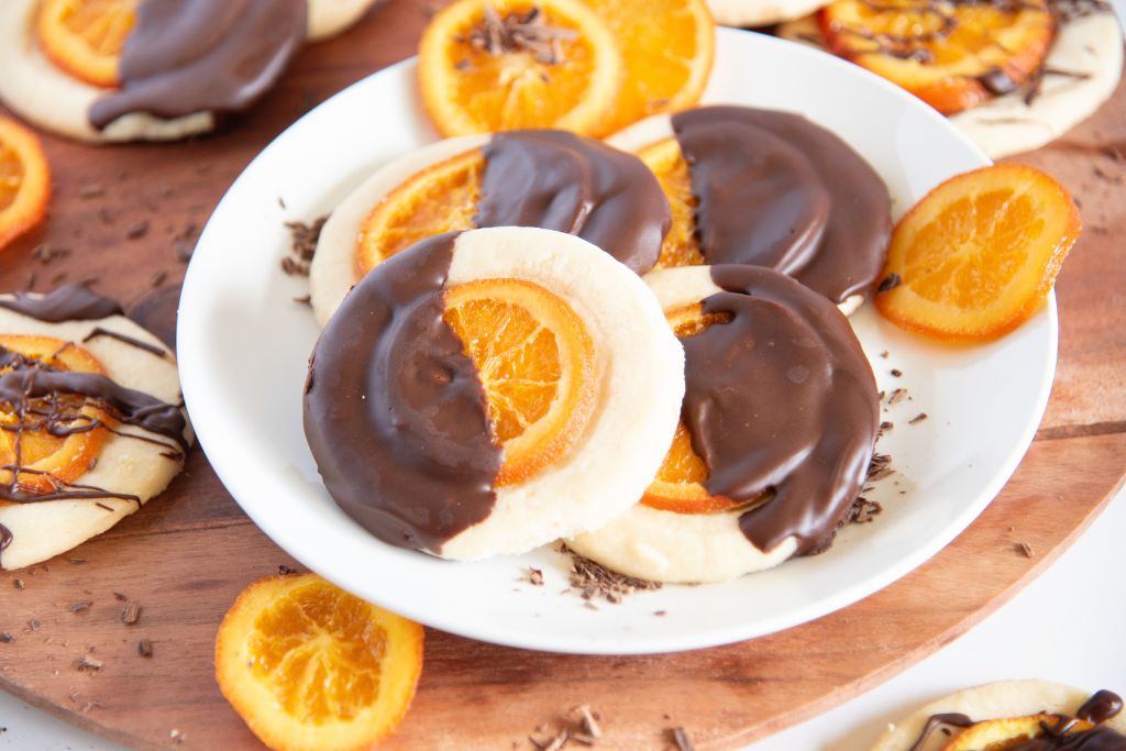 a plate of chocolate dipped shortbread cookies, there are candied oranges and more cookies around them 