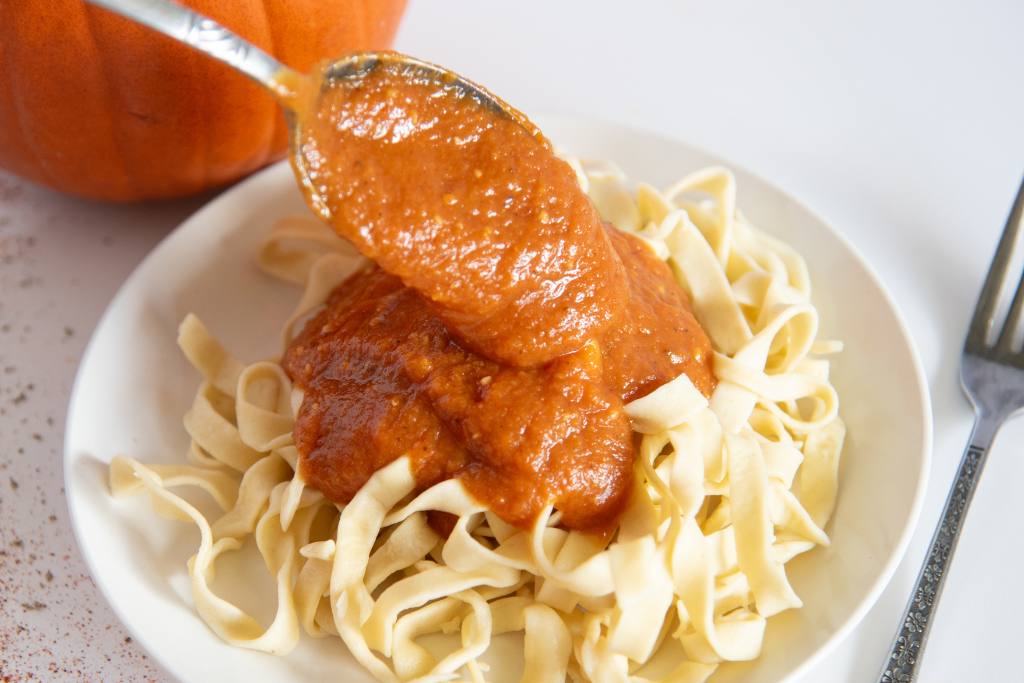 pumpkin pasta sauce being spooned over a plate of noodles
