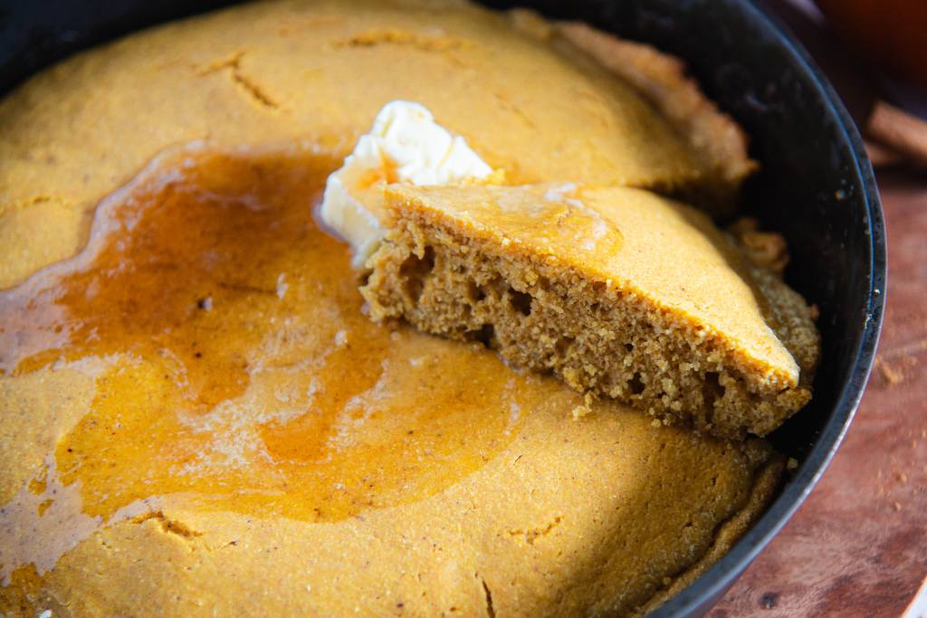 a skillet of cornbread with a slice taken out of it, the slice is resting on the rest of the uncut cornbread