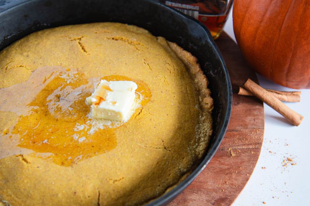 a skillet of uncut cornbread with butter and maple syrup on top 